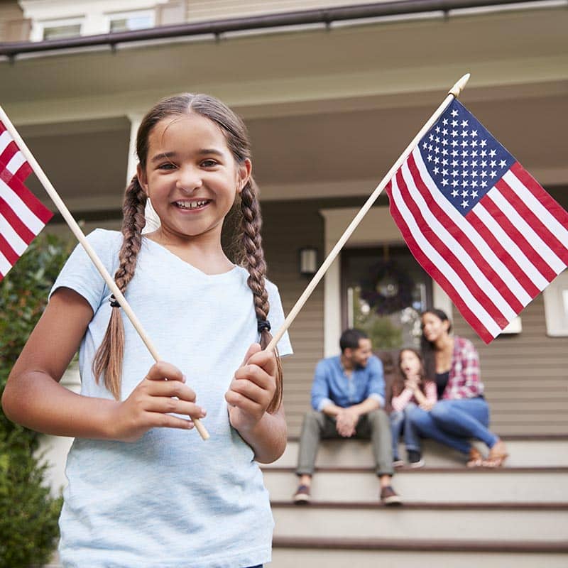 girl in braids holds two American flags outside Arizona home